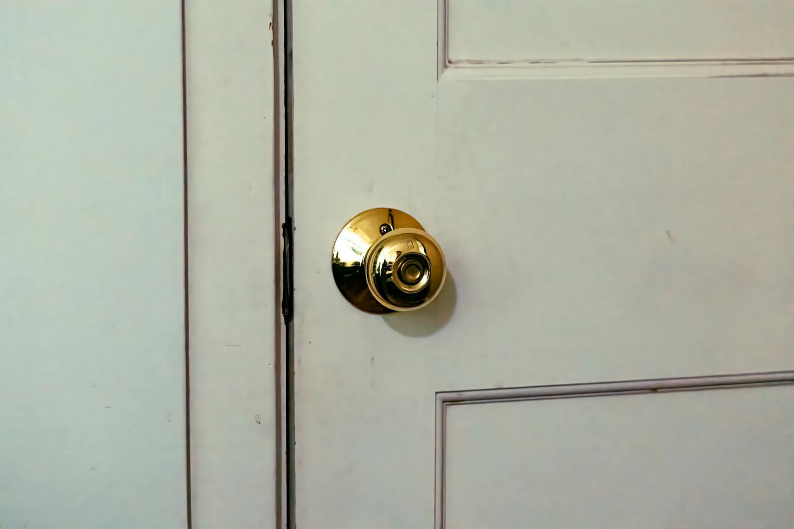 Bouton de porte sphérique en laiton doré brillant sur une porte blanche à panneaux.